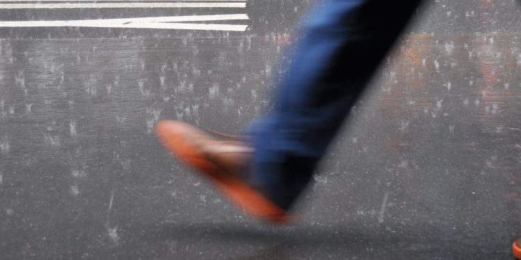an image of a person's leg and foot in blue pants and a brown/orange shoe taking a step forward on a street