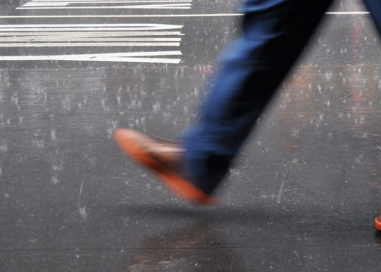 an image of a person's leg and foot in blue pants and a brown/orange shoe taking a step forward on a street
