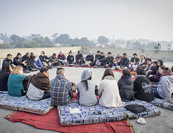a group of people sitting in a circle on cushions outside discussing something