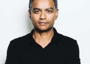 Deb Roy - a medium brown skinned man with short black hair grey at the temples wearing a black polo Tshirt, his arms crossed, looking at the camera with a subtle smile