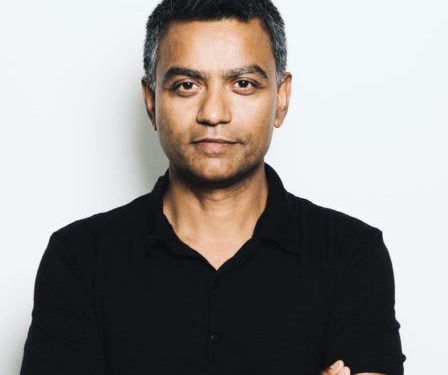 Deb Roy - a medium brown skinned man with short black hair grey at the temples wearing a black polo Tshirt, his arms crossed, looking at the camera with a subtle smile